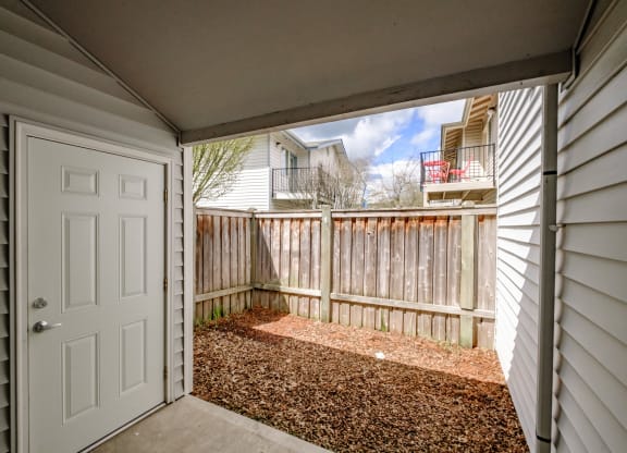 a white door opens to a small patio with a wooden fence