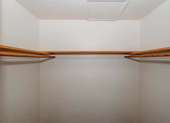 a walk in closet with white walls and wooden shelves