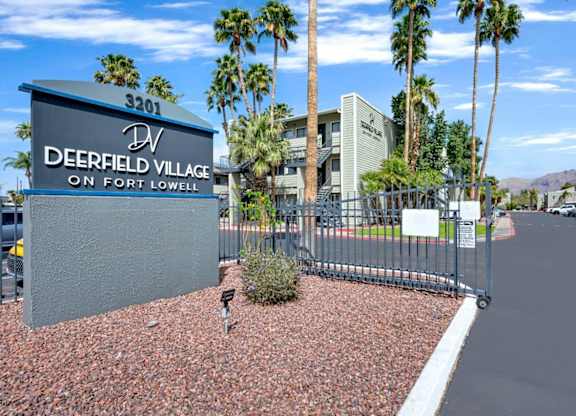 A sign for Deerfield Village on Fort Lowell stands in front of a building and palm trees.