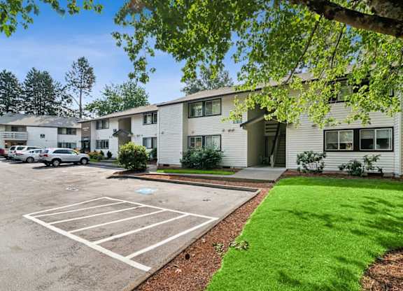 A parking lot in front of a building with a green lawn.