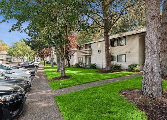 A row of cars parked on a sidewalk in front of apartment buildings.