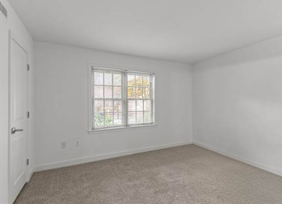 A room with a carpeted floor and a window with blinds.