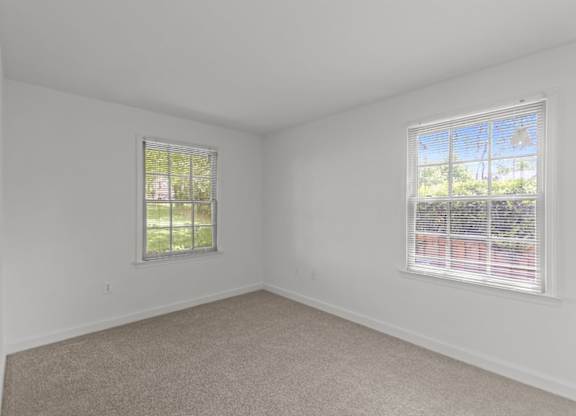 A room with two windows and carpeted floor.