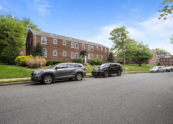 Two cars are parked on a street in front of a brick building.
