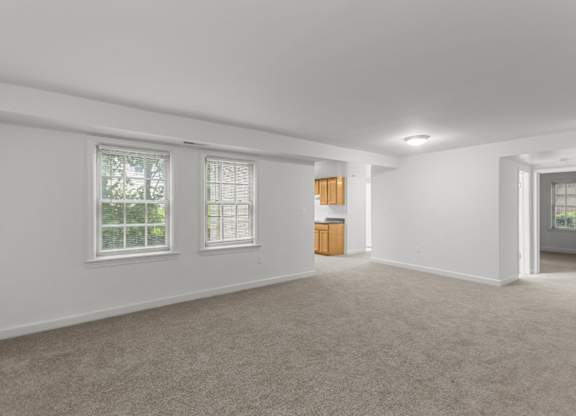 A room with a carpeted floor and two windows.