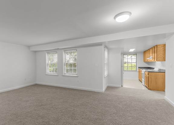 A spacious room with a carpeted floor and a window with blinds.