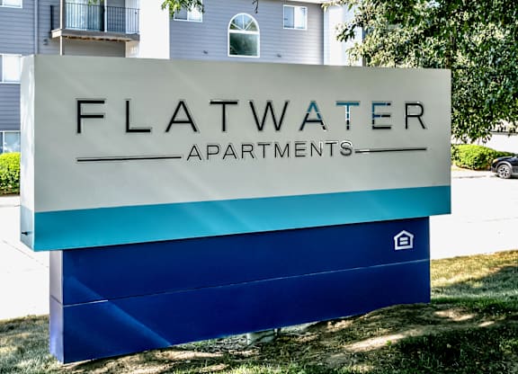 A sign for Flatwater Apartments is displayed in front of a building.