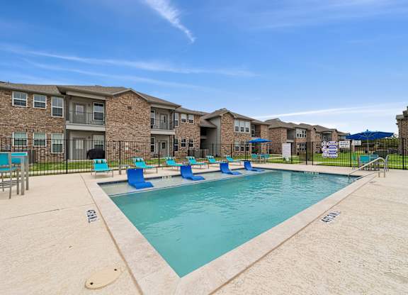 A swimming pool surrounded by a fence and chairs in front of apartment buildings.