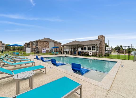 A pool area with sun loungers and a building in the background.