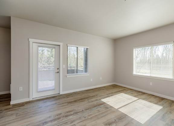 A room with a door, two windows, and a rug on the floor.