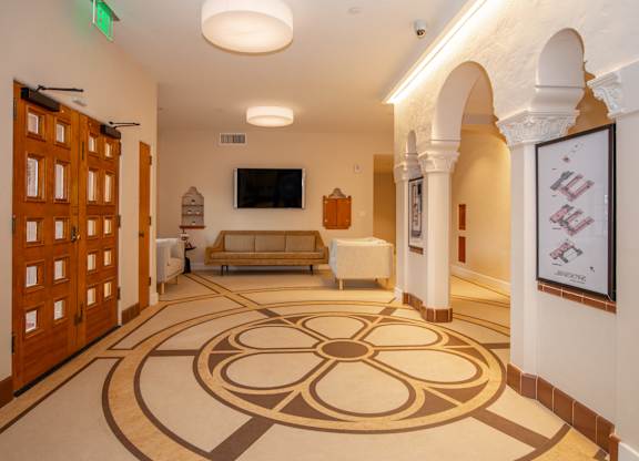 A hallway with a patterned floor and a green exit sign above the door.