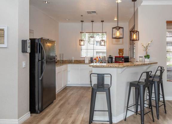 A black refrigerator stands in a kitchen with a bar area.