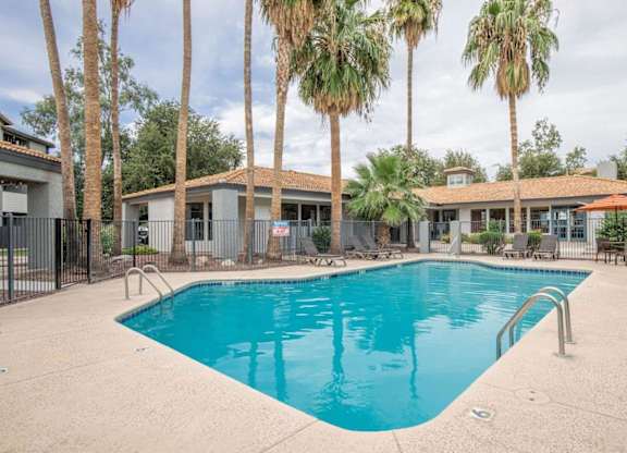 A swimming pool surrounded by palm trees and a building in the background.