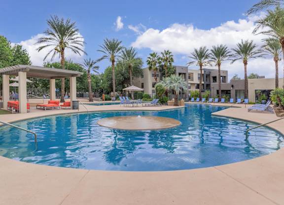 A large swimming pool surrounded by palm trees and a pavilion.
