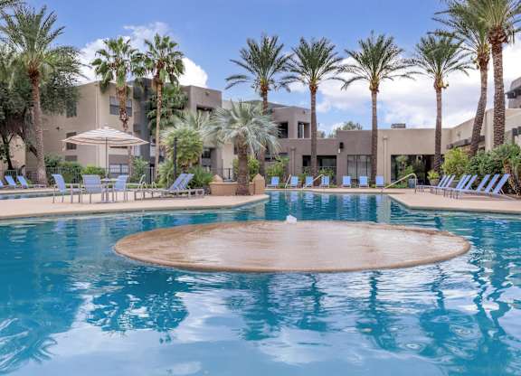 A large outdoor swimming pool surrounded by palm trees and lounge chairs.