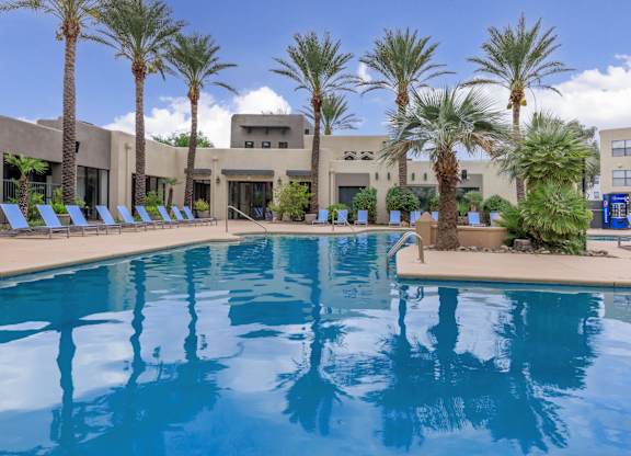 A large swimming pool surrounded by palm trees and lounge chairs.