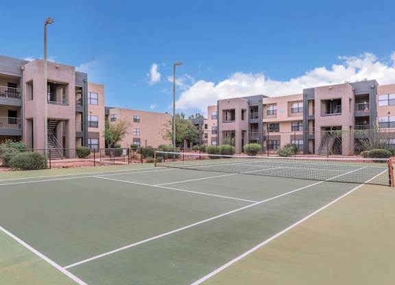 A tennis court is surrounded by apartment buildings.