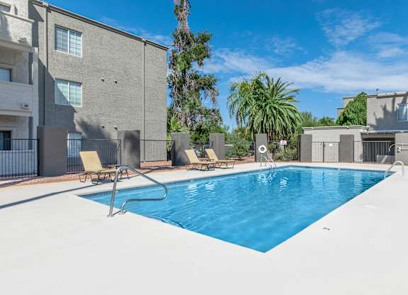 A swimming pool with lounge chairs and a building in the background.