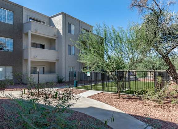 Apartment complex with a fence and trees in the front.