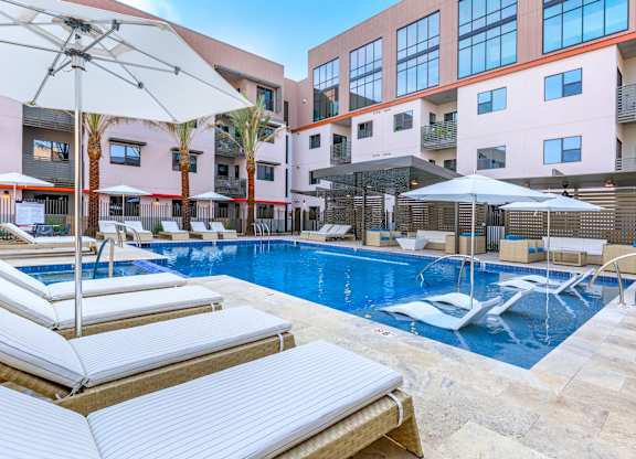 A pool with sun loungers and umbrellas in front of a building.