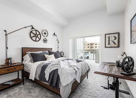 A bedroom with a large bed, a wooden table, and a window with a view of a building outside.