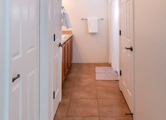 A hallway with white doors and brown tile flooring.