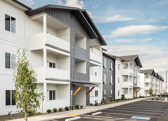 A row of modern apartment buildings with a parking lot in front.