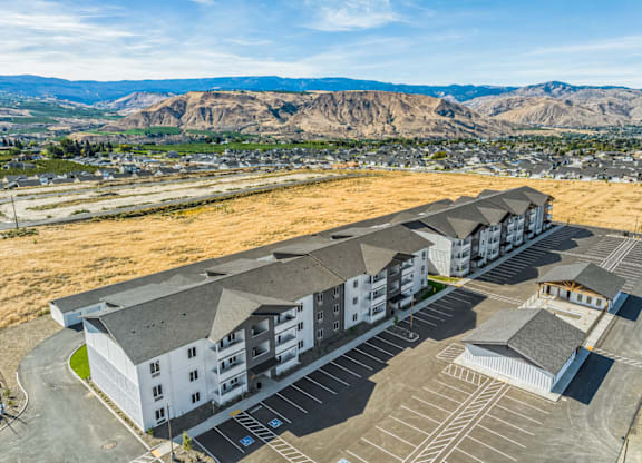 A large building complex with a parking lot in front and mountains in the background.