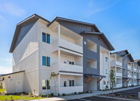 A modern apartment building with multiple balconies and a parking lot in front.
