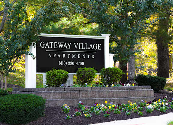 A sign for Gateway Village Apartments is displayed in front of some trees.