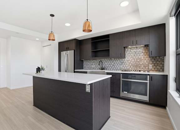 A modern kitchen with a dark island and wooden floors.