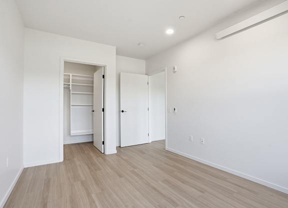 A room with a white wall and a wooden floor with a white door and a white closet.