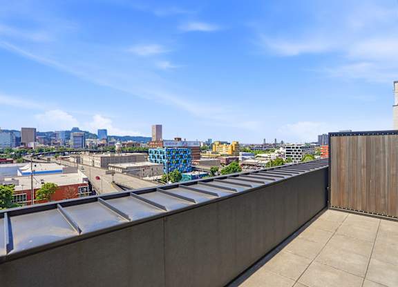 A rooftop with a metal railing and a view of a city skyline.