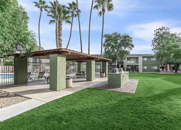 A sunny day at the poolside with palm trees and a covered seating area.