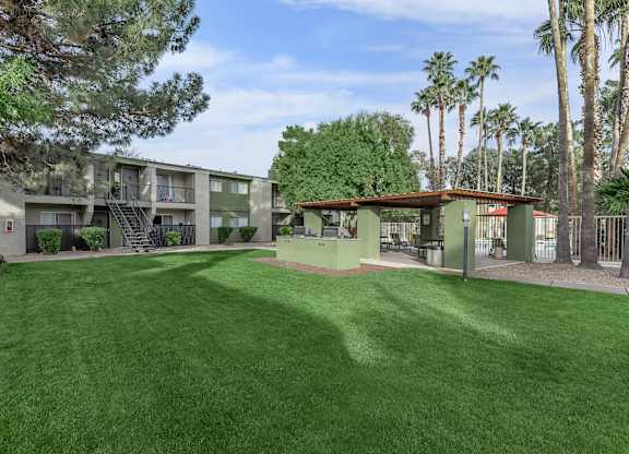 A grassy area in front of a building with palm trees in the background.