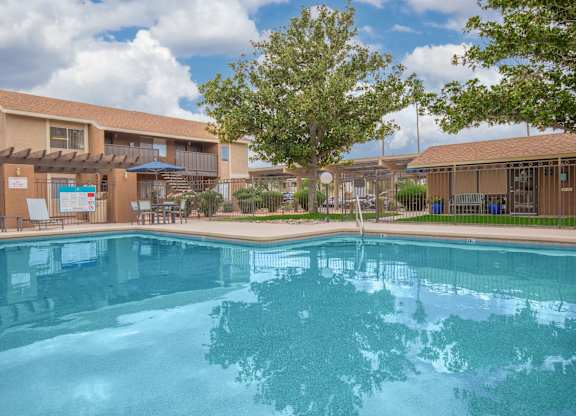 A swimming pool in front of a building with a blue sky and clouds in the background.