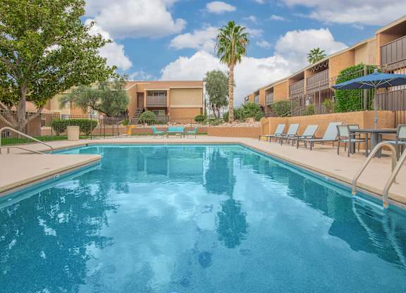 A swimming pool surrounded by lounge chairs and palm trees.