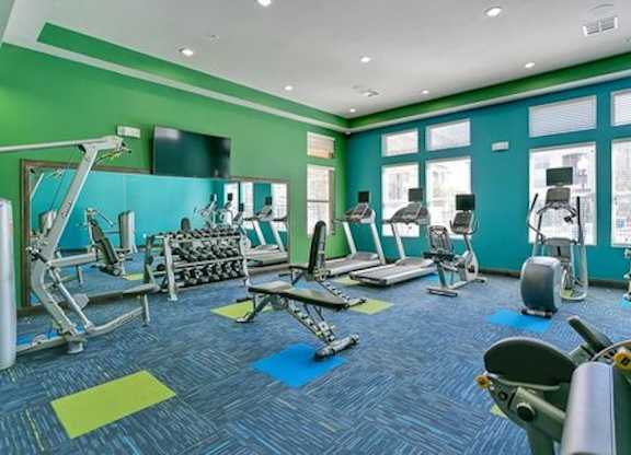 A gym with a variety of equipment including treadmills, weights, and exercise machines.