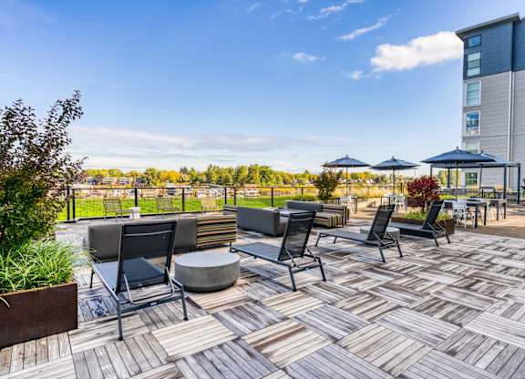 A patio with black chairs and tables is surrounded by a tall building.