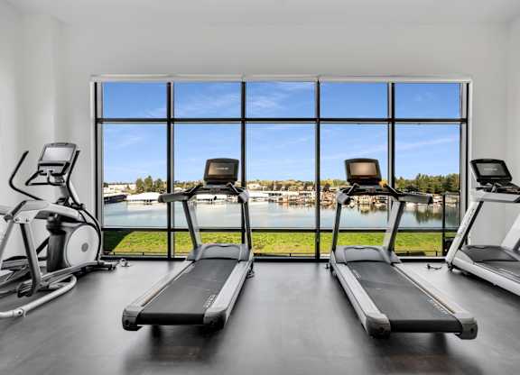 A gym with treadmills and elliptical machines with a view of the lake outside the window.