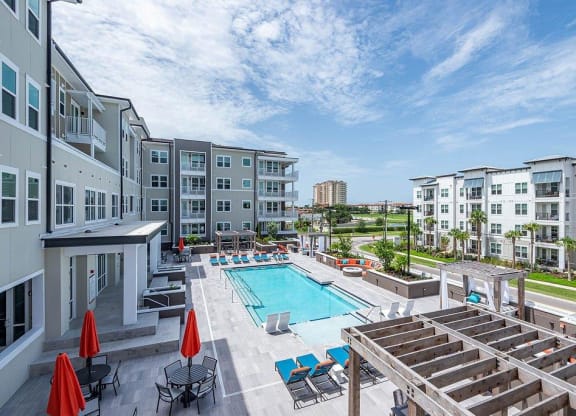 a swimming pool with lounge chairs and umbrellas in front of an apartment building