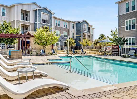 A pool area with sun loungers and a building in the background.
