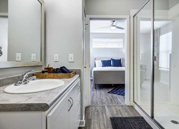 A bathroom with a sink, mirror, and a bedroom in the background.