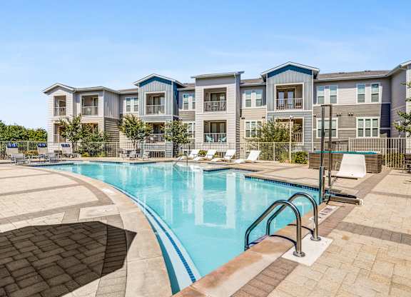 A large swimming pool is surrounded by a brick patio and a fence.