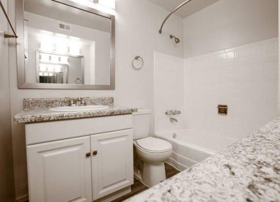A white bathroom with a marble counter top and a toilet.