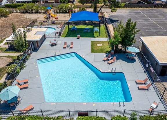 A large outdoor swimming pool surrounded by a fence and lounge chairs.