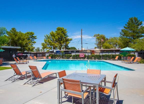 A pool with chairs and a table is surrounded by trees.