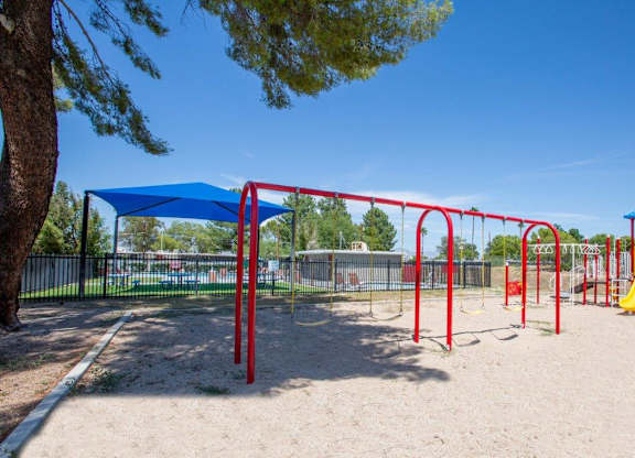 A playground with a red and yellow slide, a blue canopy, and a yellow sandbox.
