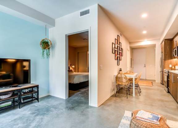 A modern living room with a television, a dining area, and a kitchen.
