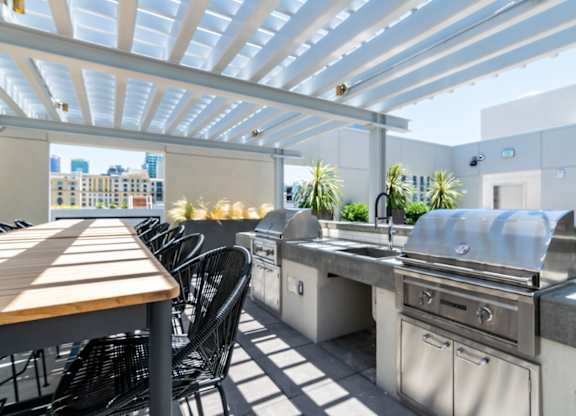 A patio with a grill and chairs under a white pergola.